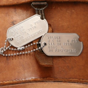 May include: Two silver military dog tags with a chain. The top tag reads "WILSON JC SR 544 26 7928 USKC L NO PREFERENCE". The bottom tag reads "WILSON JC SR 544 23 7928 USAC L NO PREFERENCE".