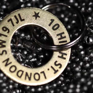 May include: A gold-colored metal keychain with the text "LONDON W19 7JL" and "10 HIGH ST" engraved on it. The keychain has a star and a small ring.