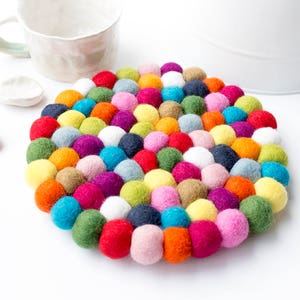 May include: A colourful round felt coaster made of many small balls of felt in various colours, including red, orange, yellow, green, blue, purple, pink, and white.