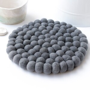 May include: A grey felt coaster made of small, round balls. The coaster is round and has a diameter of about 15 cm.