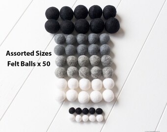 May include: Assorted Sizes Felt Balls x 50. A set of 50 felt balls in black, gray, and white. The balls are arranged in rows, with the largest balls at the top and the smallest balls at the bottom.