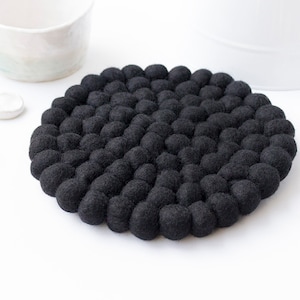 May include: A black round felt coaster with a unique texture made of small, round balls. The coaster is ideal for protecting surfaces from heat.