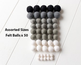 May include: Assorted Sizes Felt Balls x 50. A set of 50 felt balls in various sizes and shades of gray, black, and white. The balls are arranged in rows, starting with the largest black balls at the top and decreasing in size down to the smallest white balls at the bottom.