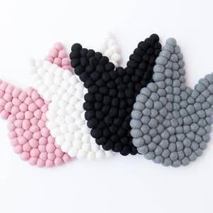 May include: Four felt flower shapes in pink, white, black, and gray. Each shape is made of small, round felt balls.