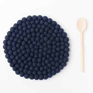 May include: A round blue felt coaster made of small balls, ideal for protecting surfaces from heat. A wooden spoon is also pictured.