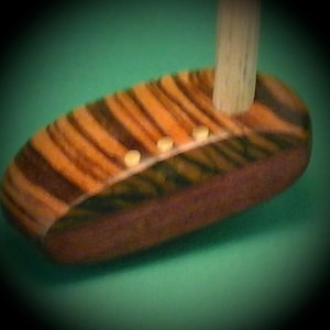 Könnte beinhalten: Ein Holz-Golfschläger mit einem gestreiften Design und vier Messing-Einsätzen. Der Schläger hat einen Holzschaft.