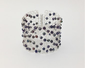 May include: A silver wire bracelet with a woven design and dark iridescent beads.