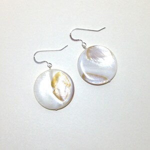 May include: A pair of silver dangle earrings with round white and gold mother of pearl shell charms.