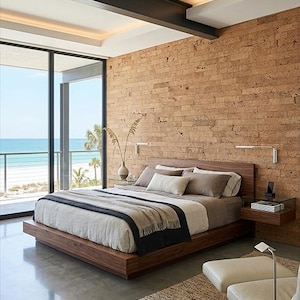 May include: A modern bedroom with a wooden bed frame and headboard. The bed is made with neutral-toned bedding and a dark gray throw blanket. A cork brick wall and large windows overlooking the ocean complete the room's design.