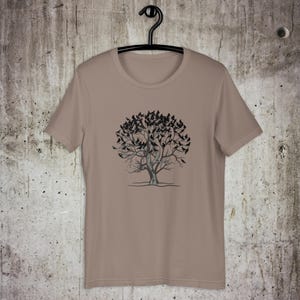 May include: A tan t-shirt with a black and white graphic of a tree with birds on the branches.
