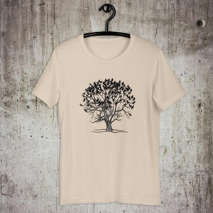 May include: A beige t-shirt with a black and white graphic of a tree with birds on the branches.