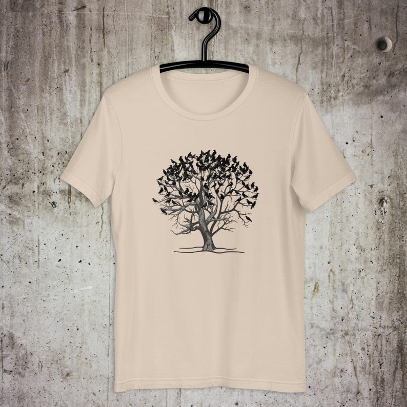 May include: A beige t-shirt with a black and white graphic of a tree with birds on the branches.