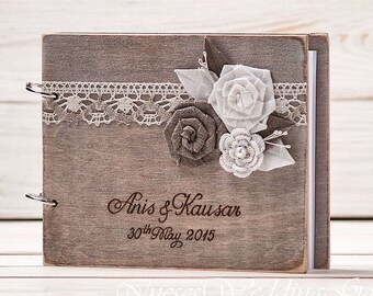 May include: A rustic wooden guest book with a lace trim and fabric flowers in shades of white and brown. The book is personalized with the names "Anis & Kausar" and the date "30th May 2015".