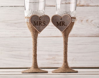 May include: Two champagne flutes decorated with burlap and lace, each with a wooden heart charm that says "MRS." and "MR."