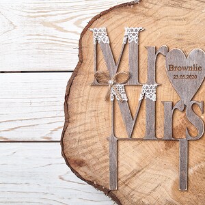 Puede incluir: Topper de pastel de madera con las palabras "Mr" y "Mrs" en un estilo r&uacute;stico. El topper presenta un coraz&oacute;n con el texto "Brownlie 23.05.2020".
