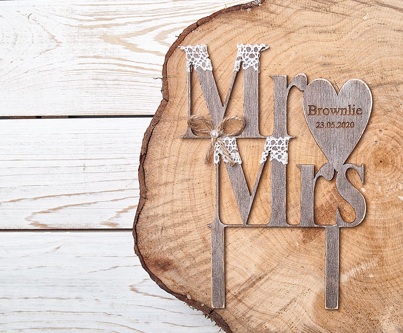 Puede incluir: Topper de pastel de madera con las palabras "Mr" y "Mrs" en un estilo r&uacute;stico. El topper presenta un coraz&oacute;n con el texto "Brownlie 23.05.2020".