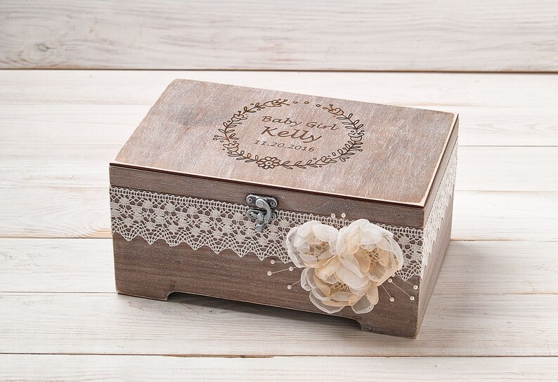 May include: A wooden keepsake box with a lace trim and a delicate flower embellishment. The lid is engraved with the text "Baby Girl Kelly 11.20.2016".