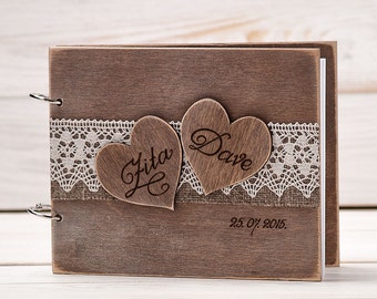 May include: A rustic wooden photo album with a lace trim and two wooden hearts with the names "Rita" and "Dave" engraved on them. The date "25.07.2015." is also engraved on the album.