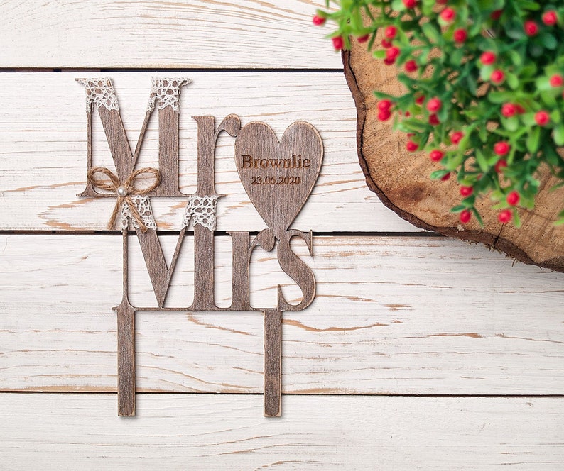 Puede incluir: Topper de pastel de madera "Mr & Mrs" con detalles de encaje y una etiqueta en forma de coraz&oacute;n que dice "Brownlie 23.05.2020".