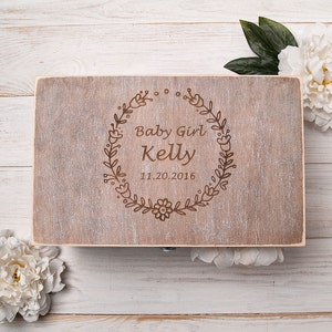 May include: A wooden box with a light brown stain and a floral design engraved on the lid. The text "Baby Girl Kelly 11.20.2016" is engraved on the lid.