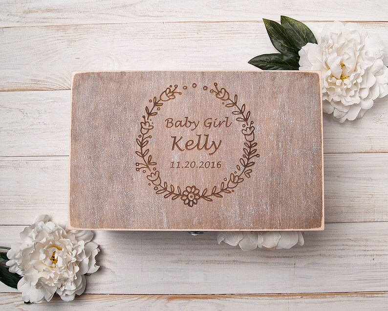 May include: A wooden box with a light brown stain and a floral design engraved on the lid. The text "Baby Girl Kelly 11.20.2016" is engraved on the lid.