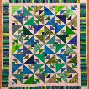 May include: A quilt with a white background and a pattern of blue and green triangles. The quilt has a border of green, blue, and white stripes.