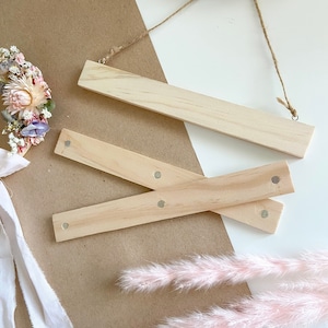 May include: Three wooden dowels with silver metal dots on the ends. The dowels are arranged in a criss-cross pattern on a white surface.