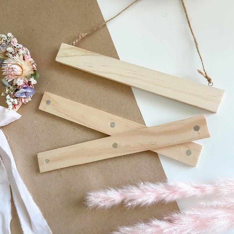 May include: Three wooden dowels with silver metal dots on the ends. The dowels are arranged in a criss-cross pattern on a white surface.