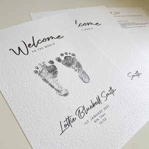 May include: A white card with black ink announcing the birth of a baby girl named Lottie Bluebell Smith. The card features a welcome message, the baby's name, birth date, weight, and time of birth. Two black ink footprints are printed on the card.