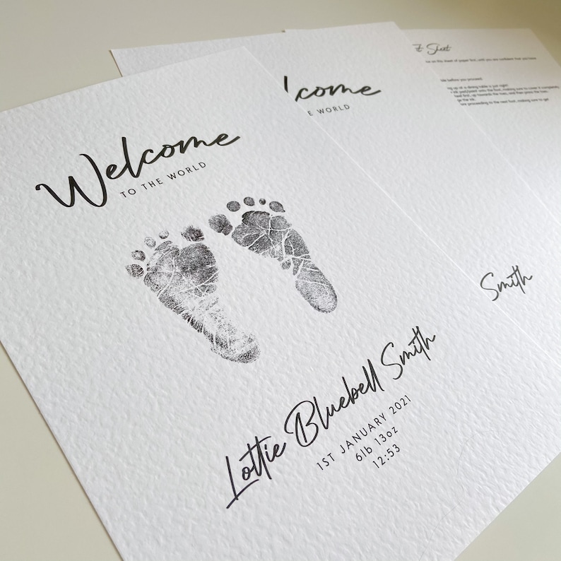 May include: A white card with black ink announcing the birth of a baby girl named Lottie Bluebell Smith. The card features a welcome message, the baby's name, birth date, weight, and time of birth. Two black ink footprints are printed on the card.