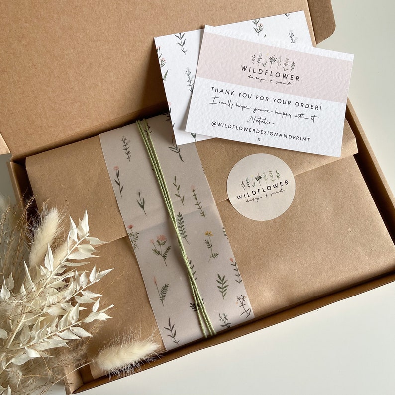 May include: A brown cardboard box with a white thank you card that says "Thank you for your order! I really hope you're happy with it. Natalie @WILDFLOWERDESIGNANDPRINT" and a white sticker with the text "WILDFLOWER design & print". The box is wrapped in brown paper with a floral pattern and a green ribbon.