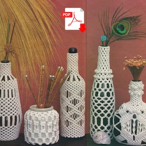 May include: Four white crocheted bottle covers with different patterns. The covers are on glass bottles, some with dried flowers and a peacock feather inside.