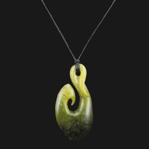May include: A green jade pendant in the shape of a traditional Maori fish hook, called a hei matau, hanging from a black cord.