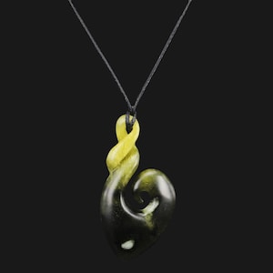 May include: A green and yellow jade pendant in the shape of a traditional Maori fish hook, called a hei matau, on a black cord.
