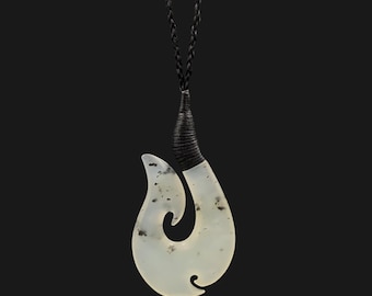 May include: A white jade fish hook pendant with black speckles, hanging from a black braided cord necklace.