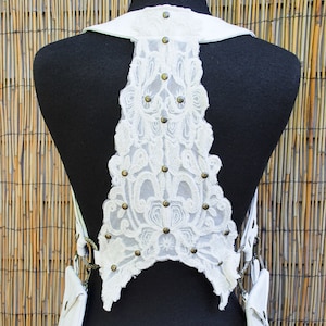 May include: White leather harness with a lace back panel and two small pockets. The lace panel is decorated with metal studs.
