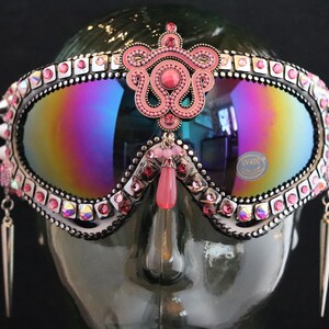 Puede incluir: Gafas de esqu&iacute; con tachuelas rosas y plateadas con un adorno de joyas rosas y pendientes colgantes. Las gafas tienen una lente iridiscente arco&iacute;ris y una etiqueta UV400.