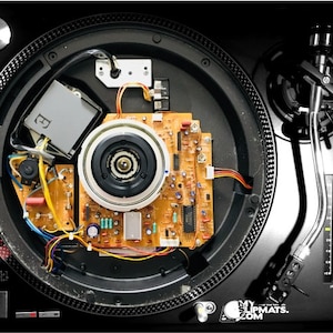 Puede incluir: Vista superior de un tocadiscos negro con componentes internos visibles. El tocadiscos presenta un brazo plateado, un control deslizante de ajuste de tono y una placa de circuito con varios componentes electrónicos. El texto "MY SLIPMATS.COM" es visible.
