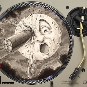 May include: A beige turntable with a black and gold tone arm. The turntable has a circular, black and white design with a drawing of a moon with a face and a rocket ship. The text "Technics" is printed on the turntable.