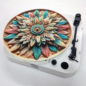 May include: A white turntable with a colorful, intricate mandala design on the record. The record features a circular pattern of feathers in shades of pink, blue, and brown.