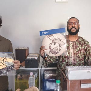 May include: Two people are holding vinyl records. The person on the left is holding a record with a cartoon illustration of a person with an elephant trunk. The person on the right is holding a record with a cartoon illustration of a person wearing a hat. The record is in a clear plastic sleeve with a blue label that says "Local Jazz".