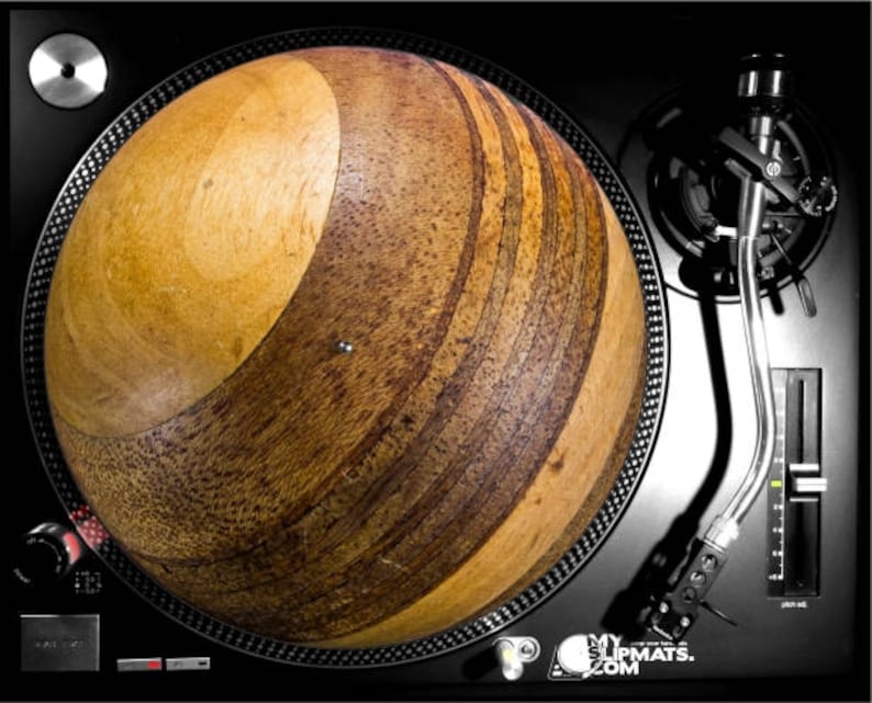 May include: A wooden turntable slipmat with a brown and light brown wood grain pattern. The slipmat is round and has a slightly raised edge. The slipmat is designed to fit on a standard turntable.