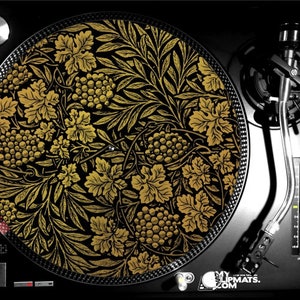 May include: A gold and black patterned turntable slipmat featuring a repeating design of grapes and leaves. The slipmat is designed to fit a standard 12-inch turntable.