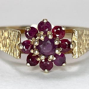 May include: A gold ring featuring a cluster of red ruby stones set in a flower design.