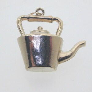 May include: A silver charm in the shape of a teapot. The teapot has a rounded body, a spout, a handle, and a lid. The charm is detailed and realistic.