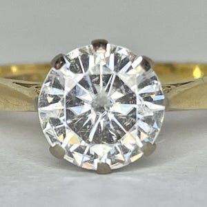 Peut inclure: Une bague en or avec un grand diamant clair de taille ronde. Le diamant est la pièce maîtresse, serti dans une monture à griffes classique. L'anneau est en or poli simple. La bague est présentée sur un fond neutre, mettant en valeur l'éclat de la pierre précieuse.