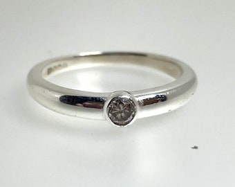 May include: A silver band ring with a single round clear gemstone set in the center.