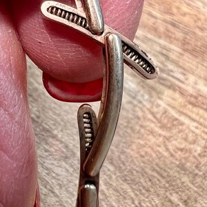 May include: A silver bracelet with a unique, intricate design featuring a cross shape. The bracelet is made of smooth, polished metal and has a delicate, textured detail.