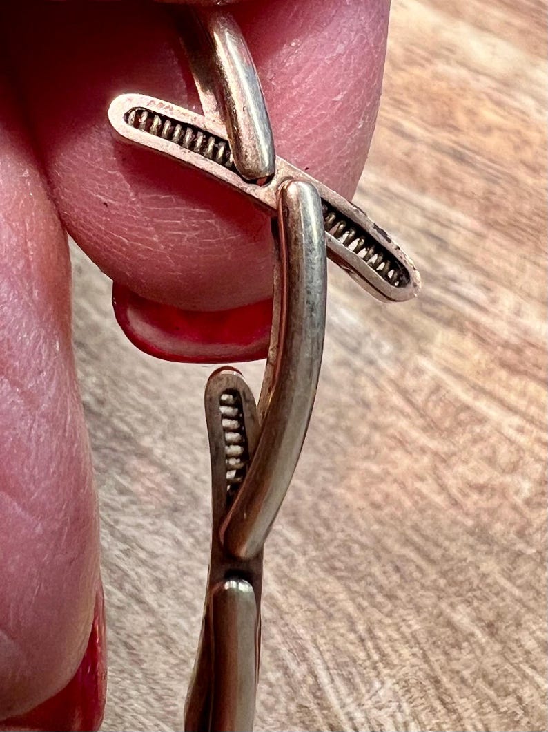 May include: A silver bracelet with a unique, intricate design featuring a cross shape. The bracelet is made of smooth, polished metal and has a delicate, textured detail.
