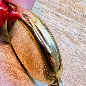 May include: A gold-toned pocket watch with a hinged lid. The watch is closed and the lid is facing the camera. The watch is on a wooden surface.